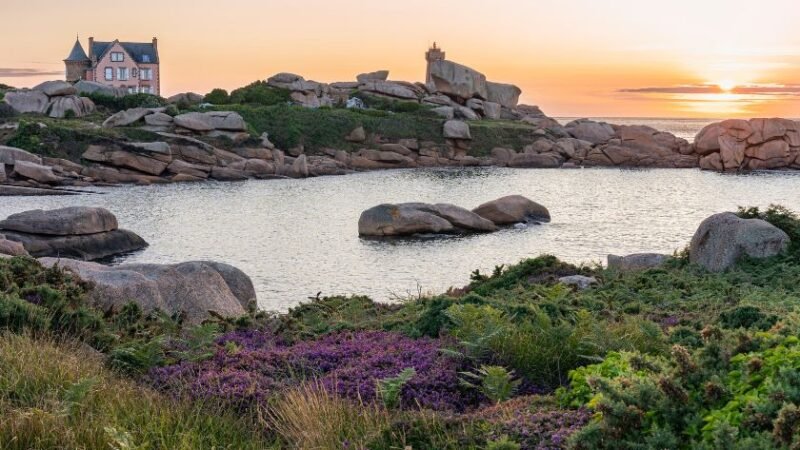 Paysage côtier avec maison, rochers et coucher de soleil sur la mer.