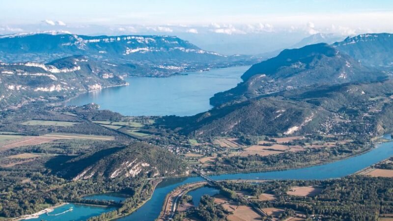 Vue aérienne d’un lac entouré de montagnes et de vallées verdoyantes.