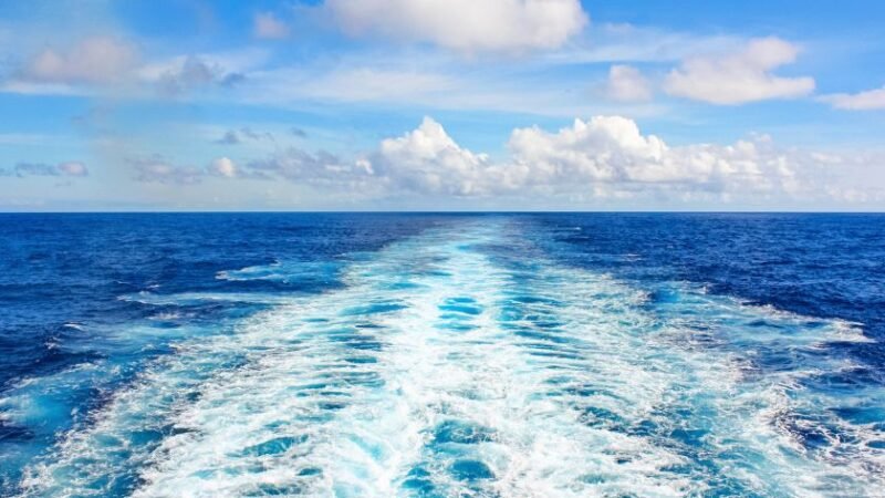 Sillage d’un bateau sur une mer bleue sous un ciel partiellement nuageux.