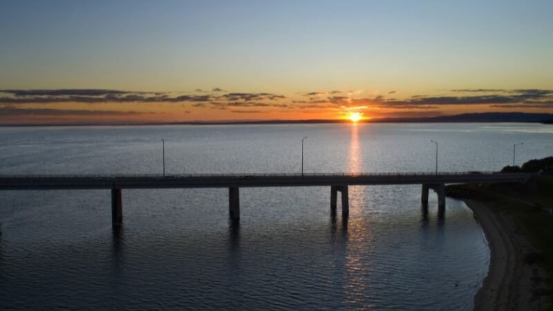 Pont traversant un plan d’eau au coucher du soleil avec horizon dégagé.