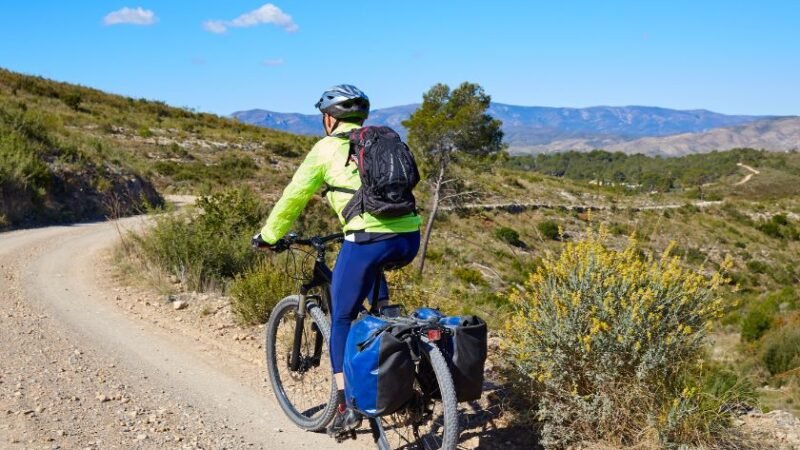 Cycliste sur une piste de montagne dans un paysage naturel, transportant des sacoches pour un voyage en autonomie.