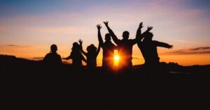 Groupe de personnes en ombres chinoises célébrant ensemble un coucher de soleil, symbolisant la joie, l’amitié et le voyage partagé en pleine nature.