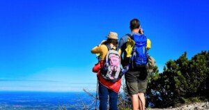 Couple de randonneurs équipés de sacs à dos admirant un paysage depuis un sommet, symbole de tourisme actif, de nature préservée et d’aventure écoresponsable.