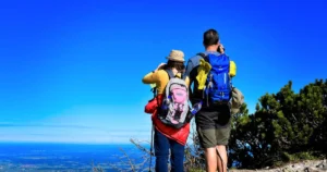 Couple de randonneurs équipés de sacs à dos admirant un paysage depuis un sommet, symbole de tourisme actif, de nature préservée et d’aventure écoresponsable.