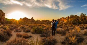 Deux randonneurs explorant un désert rocheux au coucher du soleil, entourés de végétation aride et de formations minérales, incarnant l’aventure responsable et l’écotourisme dans les paysages arides.