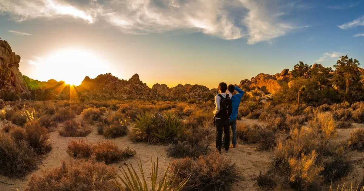 Deux randonneurs explorant un désert rocheux au coucher du soleil, entourés de végétation aride et de formations minérales, incarnant l’aventure responsable et l’écotourisme dans les paysages arides.