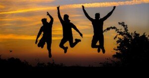 Silhouettes de trois personnes sautant de joie au coucher du soleil, symbolisant la liberté, l’amitié et l’énergie positive en pleine nature.