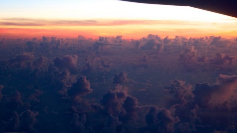 Vue aérienne d’un ciel rempli de nuages au coucher du soleil, prise depuis un avion en vol.
