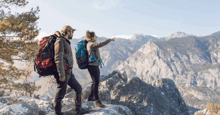 Couple de randonneurs avec sacs à dos observant les montagnes depuis un sommet rocheux, symbole d’aventure, de tourisme responsable et de connexion à la nature.