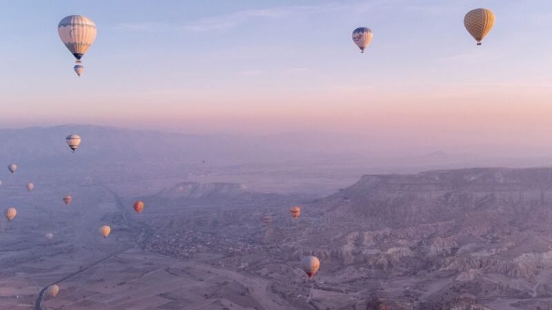 Montgolfières colorées flottant dans le ciel au lever du soleil au-dessus d’un paysage désertique et vallonné.