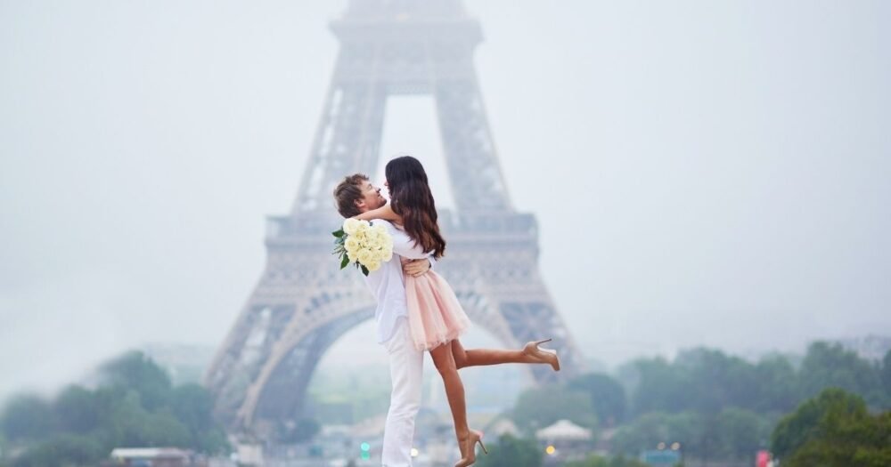 Couple romantique s'enlaçant devant la tour Eiffel par une matinée brumeuse à Paris, symbolisant l’amour éternel dans la Ville Lumière.
