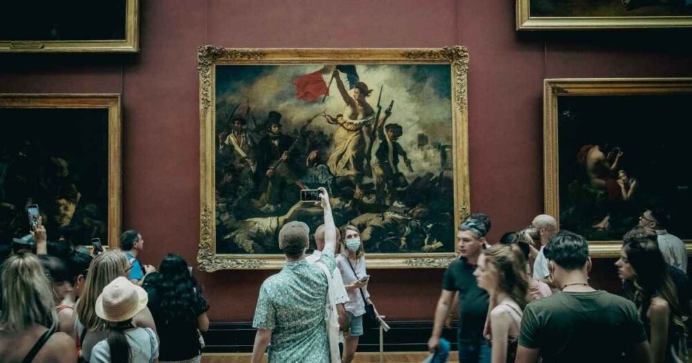 Visiteurs admirant le tableau "La Liberté guidant le peuple" de Delacroix au musée du Louvre, une immersion au cœur de l’art et de l’histoire française.