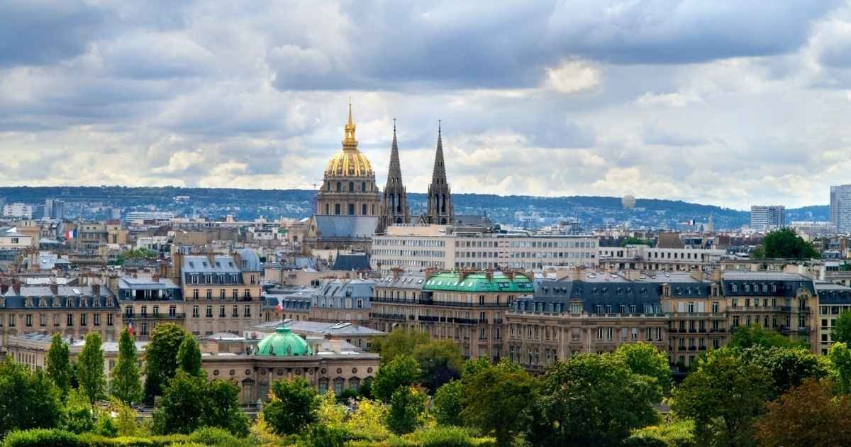 Vue panoramique des toits parisiens avec en arrière-plan le Dôme des Invalides et les flèches gothiques de l’église Saint-Augustin, capturant le charme architectural de Paris.