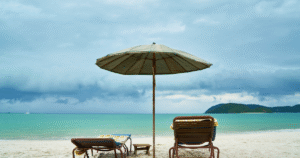 Transats vides sous un parasol en bord de mer turquoise, face à l’horizon nuageux, évoquant une pause paisible sur une plage tropicale avant la pluie.