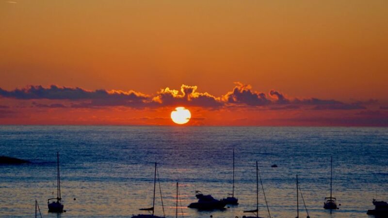 Coucher de soleil vibrant sur la mer avec plusieurs bateaux amarrés, créant une ambiance paisible.