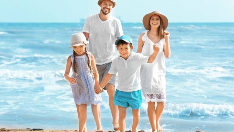 Famille heureuse marchant sur la plage au bord de la mer pendant les vacances d’été, sous le soleil du Maroc.